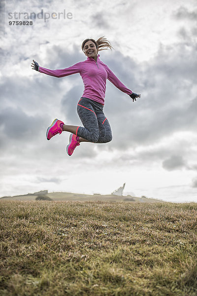 Spanien  Gijon  sportliche junge Frau beim Springen auf der Wiese