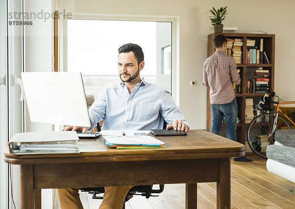 Junger Mann  der zu Hause am Computer arbeitet