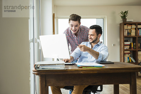 Zwei lächelnde junge Männer schauen auf den Computerbildschirm.