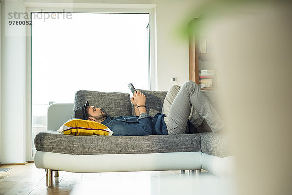 Mann auf dem Sofa liegend mit digitalem Tablett