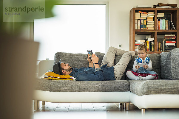 Vater und Tochter mit digitalem Tablett und Smartphone auf Sofa