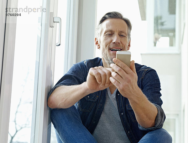 Deutschland  Köln  Erwachsener Mann am Fenster sitzend mit Smartphone