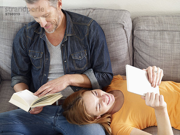Erwachsener Mann mit erwachsener Tochter beim Lesen auf dem Sofa