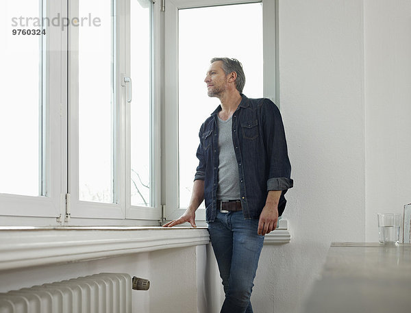 Deutschland  Köln  Erwachsener Mann am Fenster stehend  aus dem Fenster schauend