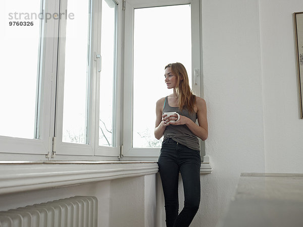 Deutschland  Köln  Junge Frau steht am Fenster  schaut hinaus