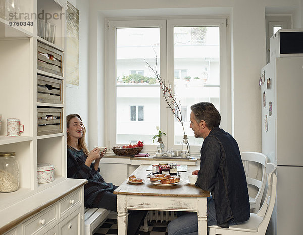 Junge Frau und reifer Mann sitzen in der Küche und frühstücken.
