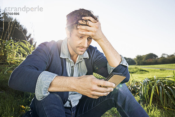 Mann sitzt auf einer Wiese und liest SMS