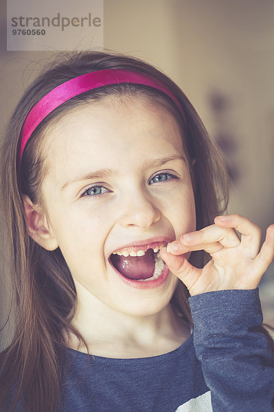 Porträt eines lächelnden Mädchens mit Zahnlücke  das Milchzahn in der Hand hält.
