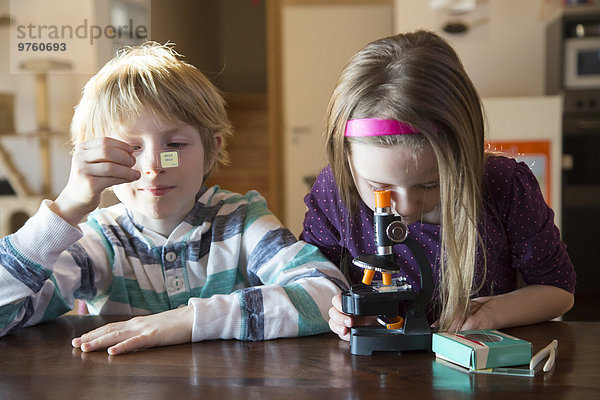Bruder und Schwester mit Mikroskop zu Hause