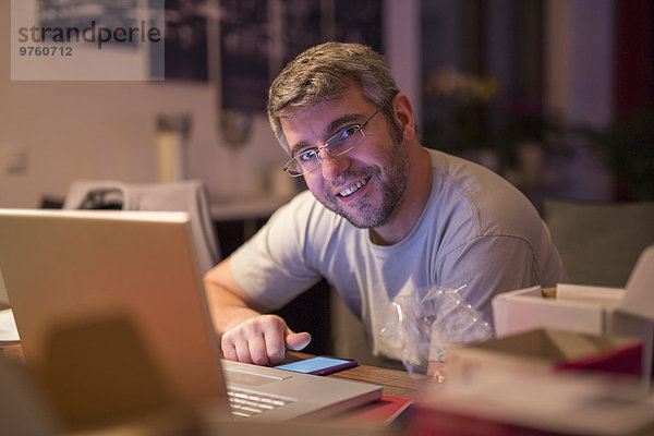 Lächelnder Mann mit Laptop und Smartphone am Schreibtisch