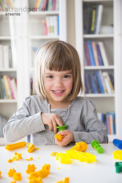 Porträt eines lächelnden kleinen Mädchens  das mit gelbem Knetmasse spielt.