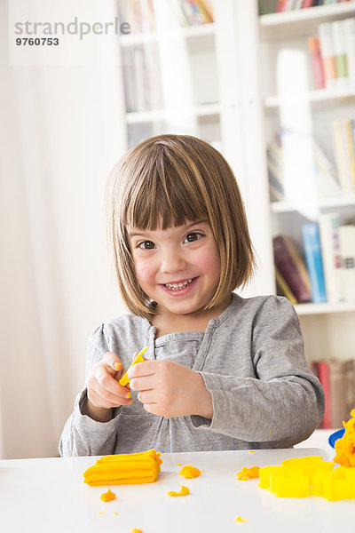 Porträt eines glücklichen kleinen Mädchens  das mit gelber Knetmasse spielt.