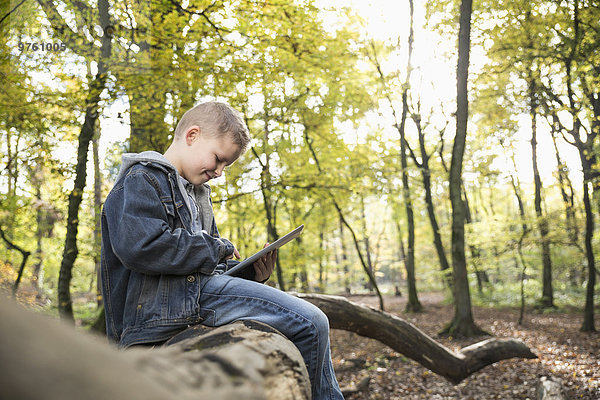 Deutschland  lächelnder kleiner Junge mit digitalem Tablett im Wald