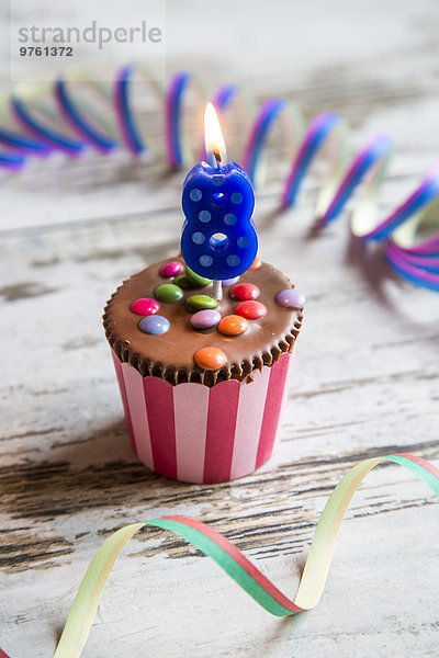 Geburtstagsmuffin mit Schokoladenknöpfen und angezündeter Kerze