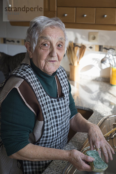 Porträt der Seniorin beim Geschirrspülen in der Küche