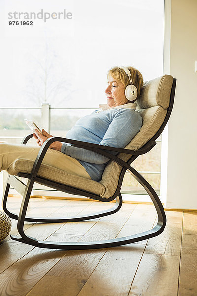 Seniorin zu Hause mit Kopfhörer und digitalem Tablett