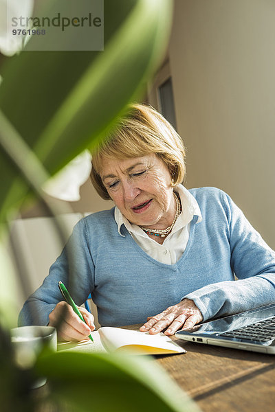 Seniorin zu Hause mit Laptop und Notebook