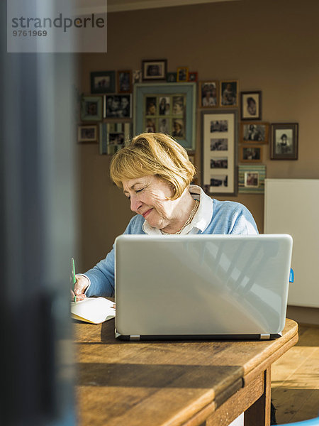 Seniorin zu Hause mit Laptop und Notebook