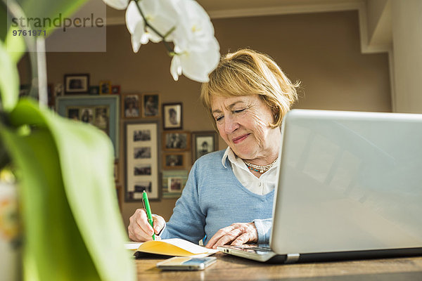 Seniorin zu Hause mit Laptop und Notebook