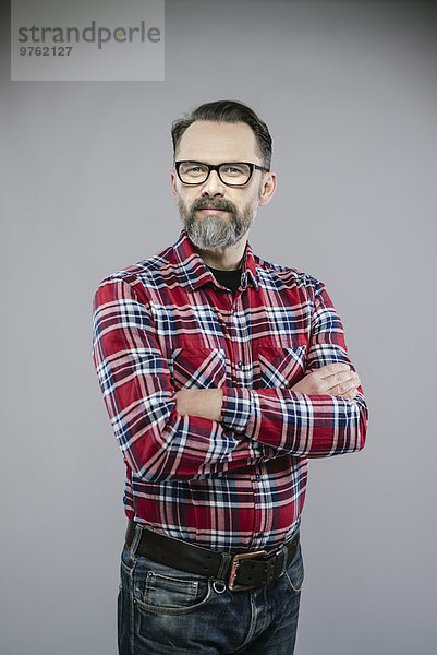 Porträt eines Mannes mit Bart und Brille  die die Arme kreuzen.