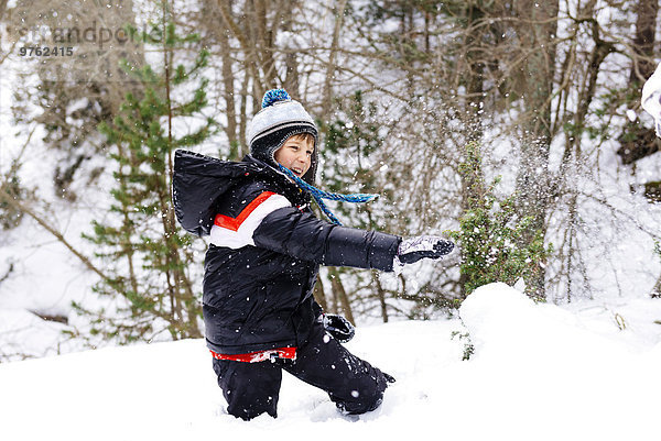 Glücklicher Junge spielt mit Schnee im Wald