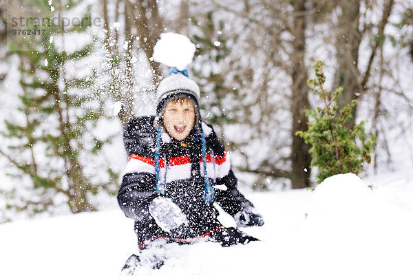 Glücklicher Junge  der einen Schneeball in den Wald wirft.
