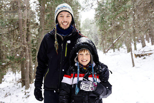 Glücklicher Mann und Junge im Wald beim Schneefall