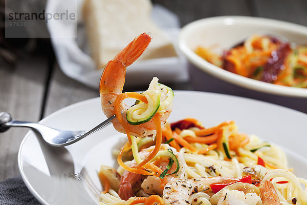Spaghetti mit Scampis und Gemüse auf Teller  Karotten- und Zucchinispiralen  Gabel  Nahaufnahme