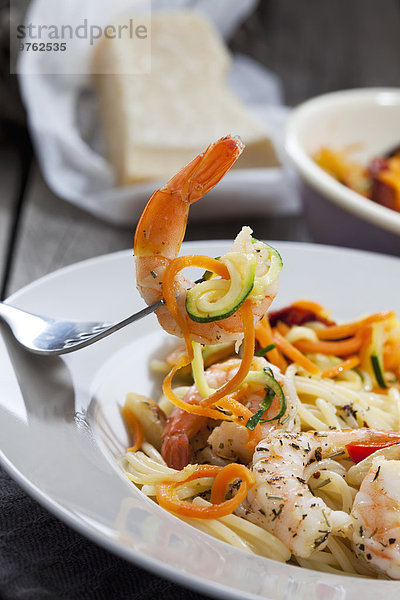 Spaghetti mit Scampis und Gemüse auf Teller  Karotten- und Zucchinispiralen  Gabel  Nahaufnahme