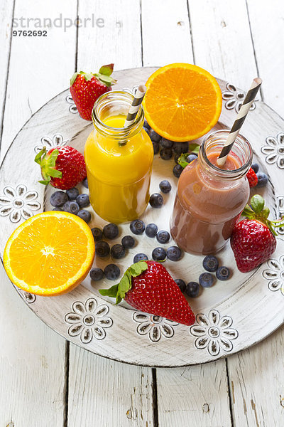 Orangen- und Erdbeer-Smoothie in Glasflaschen und Früchten auf dem Teller