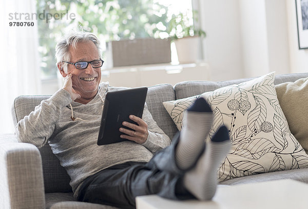 sitzend Senior Senioren benutzen Mann Computer lächeln Zimmer Couch Wohnzimmer Tablet PC