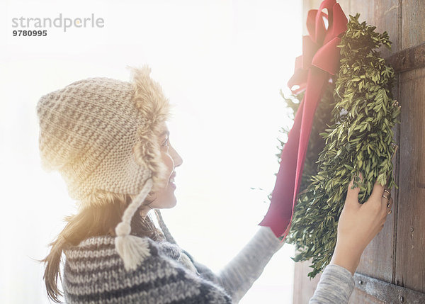 junge Frau junge Frauen Eingang Tür hängen Weihnachten Ansicht Blumenkranz Kranz Seitenansicht