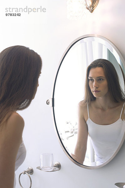 Frau betrachtet sich selbst im Badezimmerspiegel