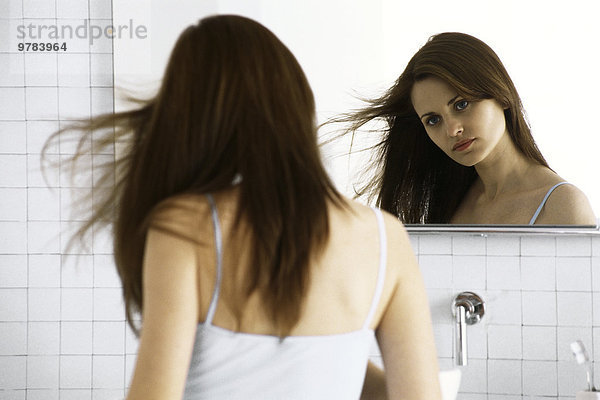 Junge Frau schaut in den Spiegel  trocknet die Haare.