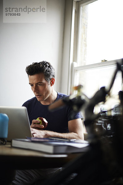 Mann arbeitet am Laptop zu Hause essen Apfel