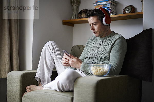 Mann im Sessel sitzend mit Kopfhörer über Smartphone