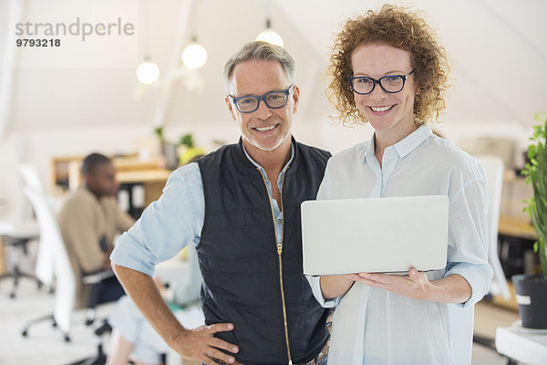 Portrait von Mann und Frau mit Laptop  lächelnd im Büro