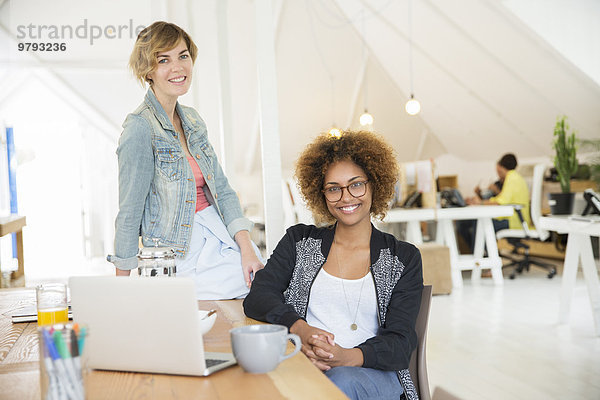 Portrait von lächelnden Frauen im Büro mit Laptop auf dem Schreibtisch