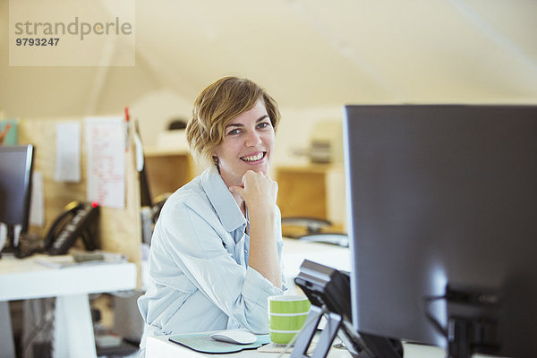 Porträt einer lächelnden Frau im Büro  am Schreibtisch sitzend mit Computer