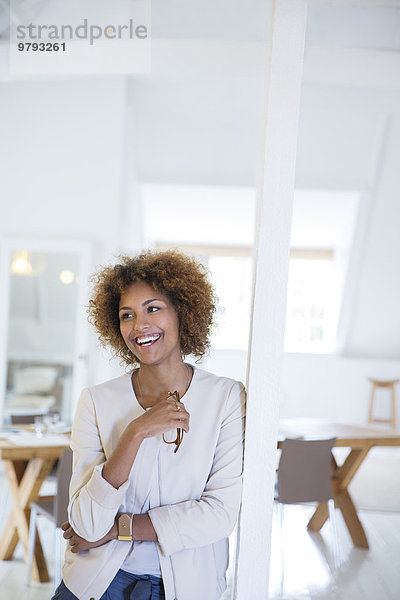 Porträt einer Frau  die sich im Büro an die Säule lehnt und lächelt
