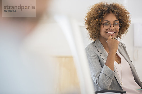 Porträt einer Frau  die im Büro sitzt  eine Brille trägt und lächelt.