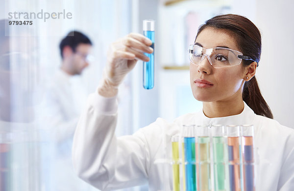 Frau im Labor betrachtet Fläschchen mit blauer Flüssigkeit