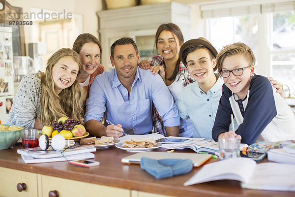 Gruppe von Teenagern mit einem erwachsenen Mann am Tisch im Esszimmer
