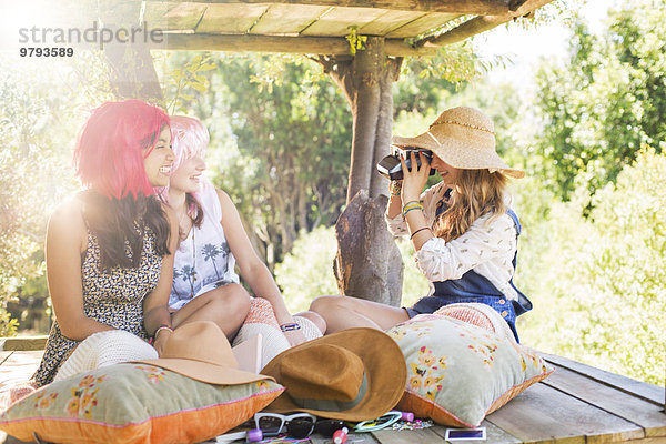Drei Teenagermädchen fotografieren im Baumhaus im Sonnenlicht