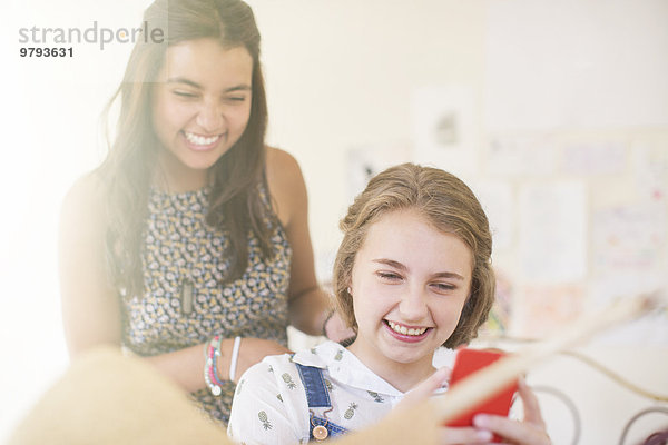 Zwei Mädchen im Teenageralter teilen sich Smartphone und lächeln