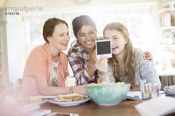 Drei Mädchen im Teenageralter  die beim Sitzen am Tisch ein Foto ansehen