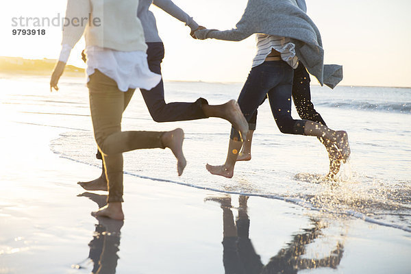 Gruppe von vier Freunden  die Händchen halten und am Strand rennen.