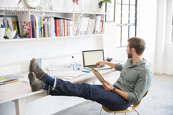 Porträt eines jungen Mannes mit Beinen auf dem Schreibtisch bei der Arbeit mit dem Laptop