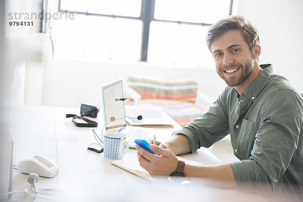 Porträt eines jungen Mannes am Schreibtisch mit Handy und Laptop