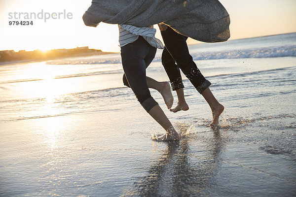 Beine eines jungen Paares  das bei Sonnenuntergang am Strand läuft.